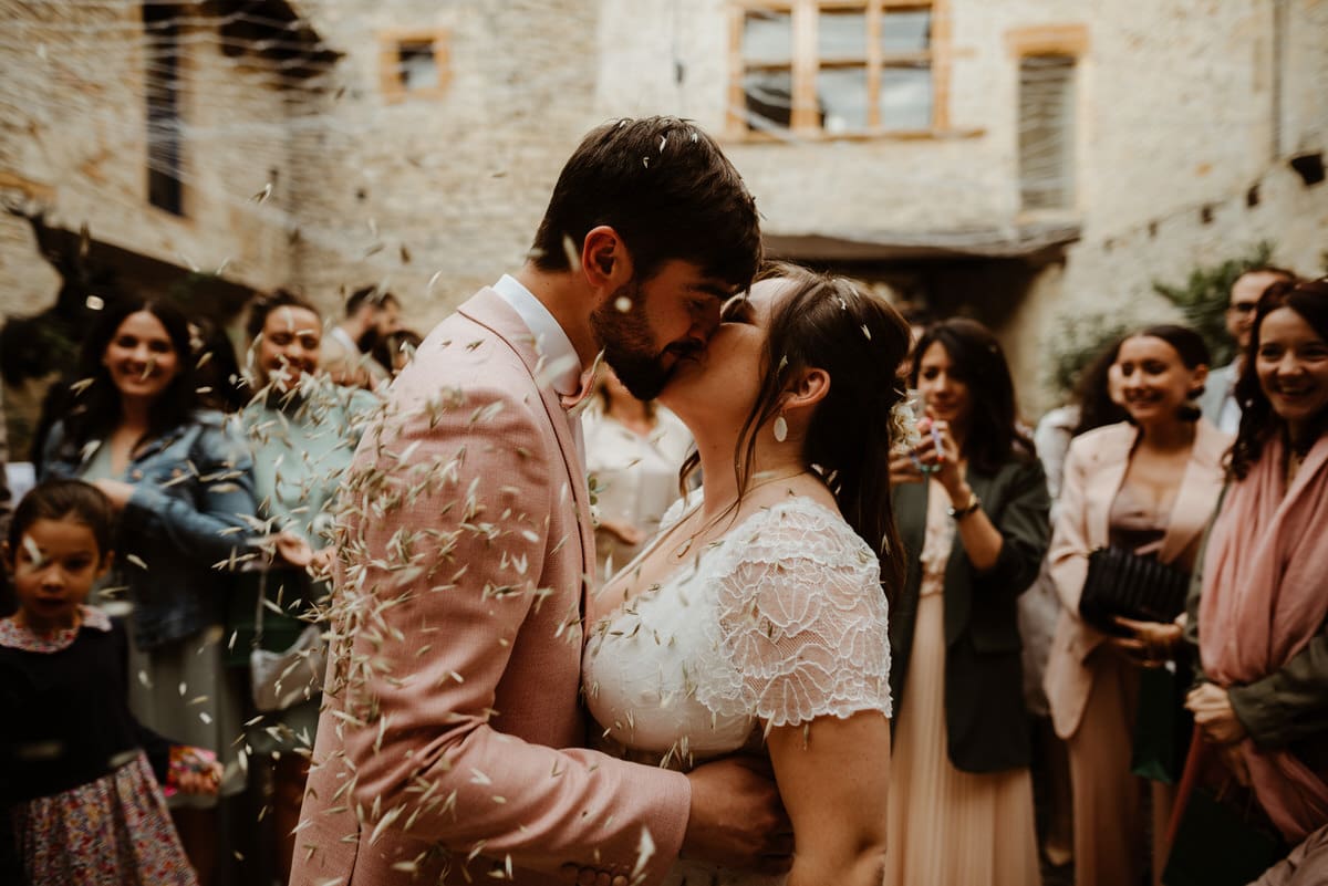 Mariés s'embrassant au milieu d'une haie d'honneur d'invités leur lançant des pétales de fleurs séchées